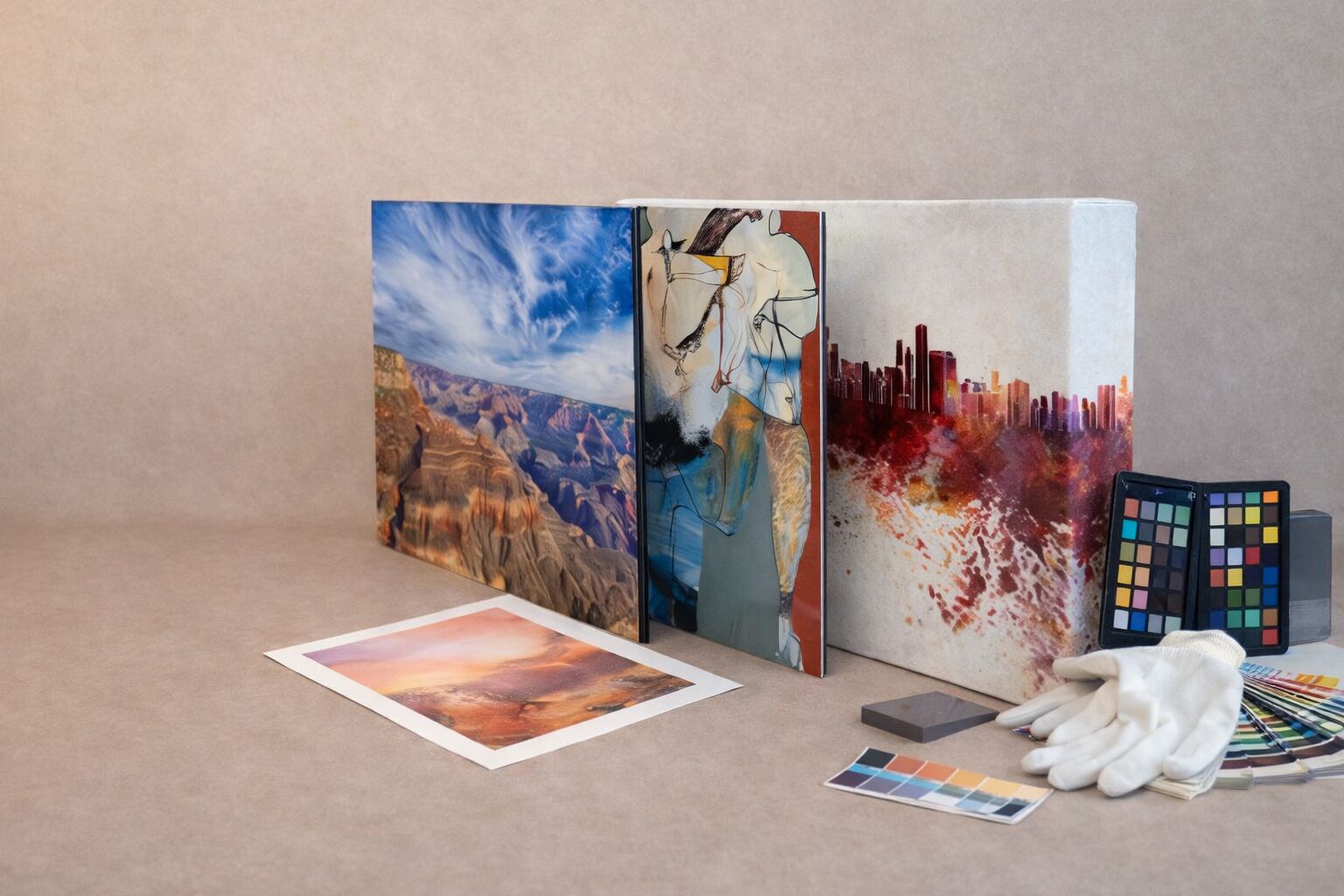 Fine art print studio product display with a giclee paper print, canvas wrap, acrylic print, and metal art print, alongside white cotton gloves and a color calibration chart on a neutral tabletop.